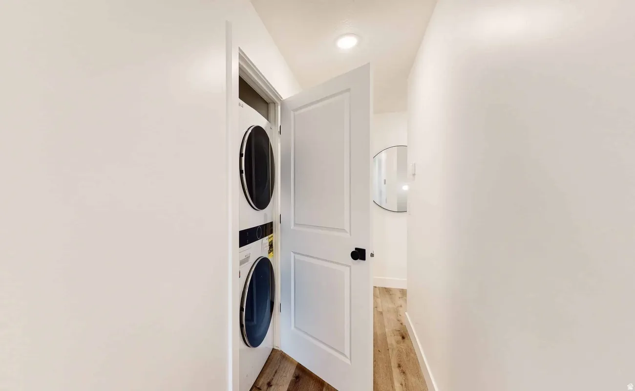 Integrated laundry closet featuring a stacked washer and dryer, white paneled door with black hardware, and recessed lighting