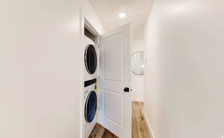 Integrated laundry closet featuring a stacked washer and dryer, white paneled door with black hardware, and recessed lighting