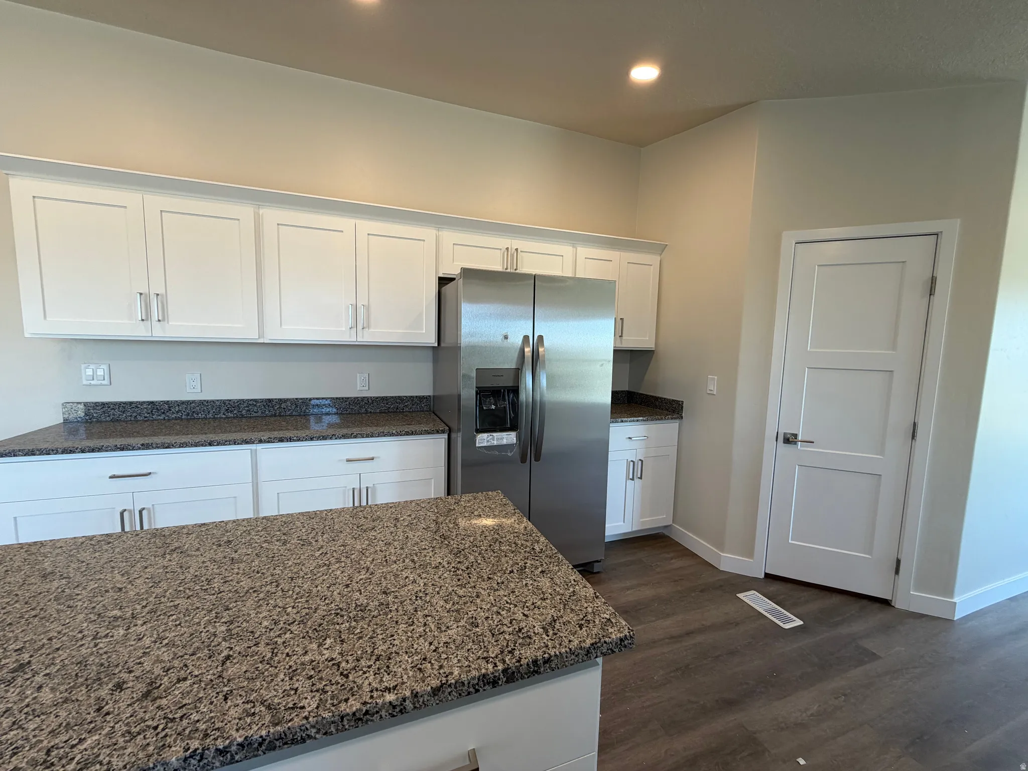 Kitchen featuring white shaker cabinetry, speckled countertops, stainless steel refrigerator, and wood-finish flooring
