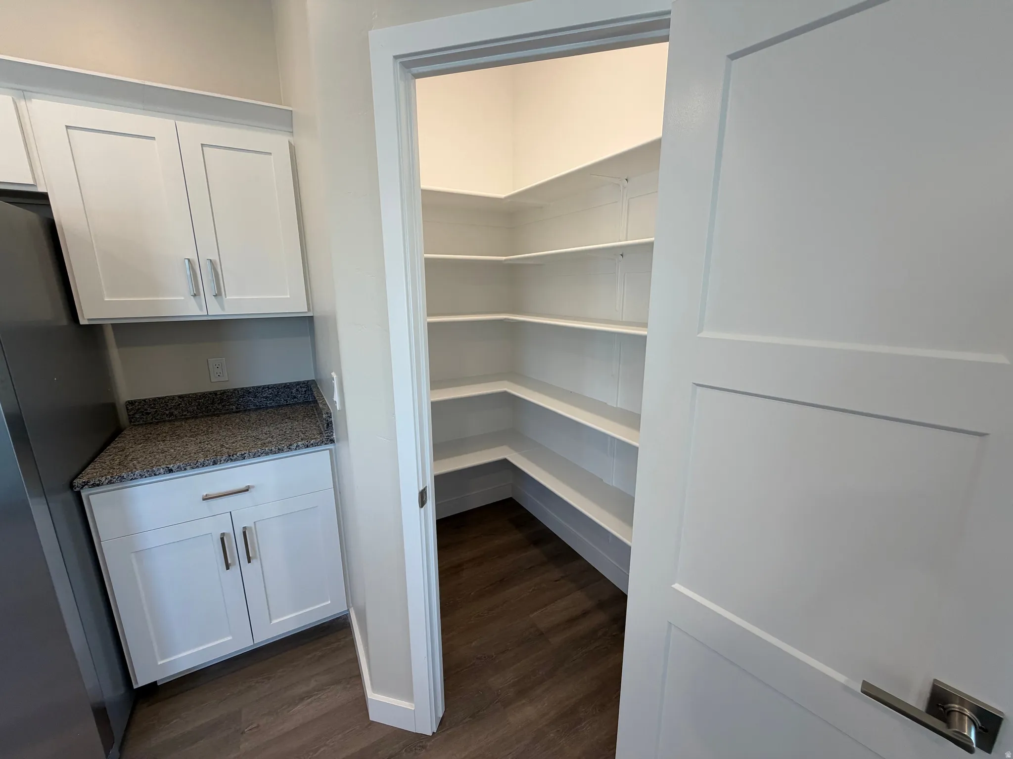 Expansive corner pantry featuring multiple white built-in shelves and wood-finish flooring