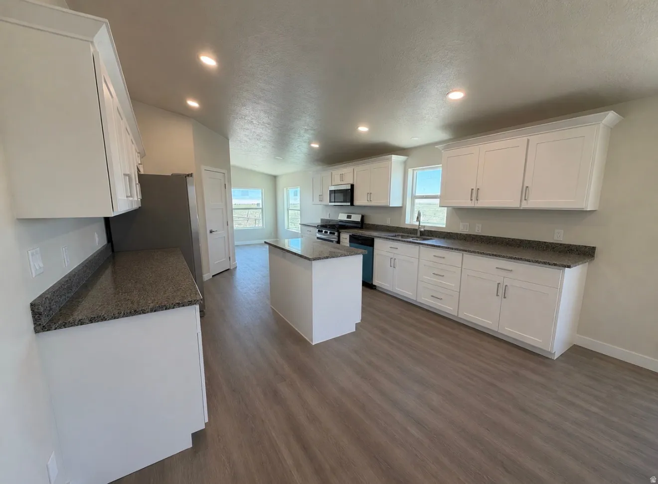 Spacious kitchen featuring white cabinetry, dark stone countertops, stainless steel appliances, a central island, and wood-finish flooring