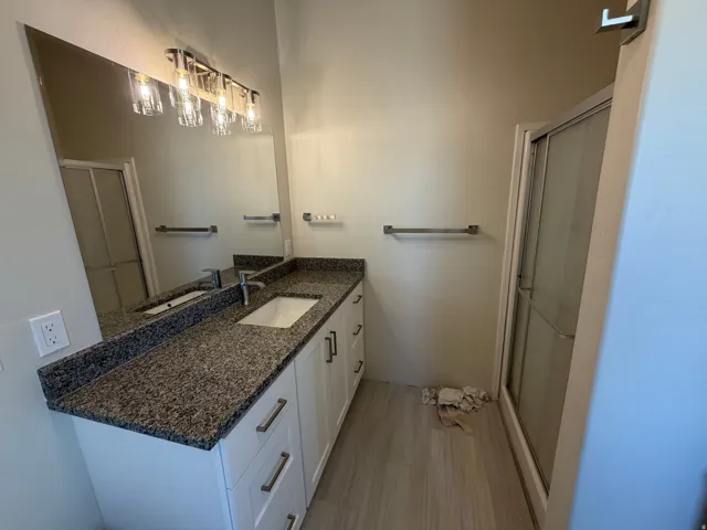 Dual sink vanity with a speckled countertop, white cabinetry, and brushed nickel hardware