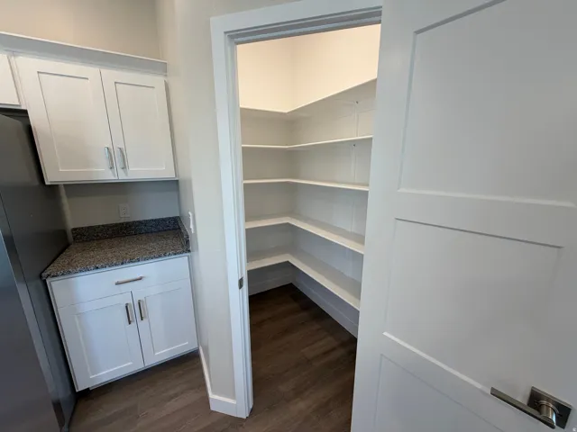 Expansive corner pantry featuring multiple white built-in shelves and wood-finish flooring