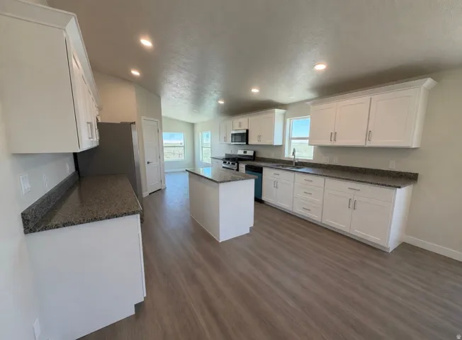Spacious kitchen featuring white cabinetry, dark stone countertops, stainless steel appliances, a central island, and wood-finish flooring