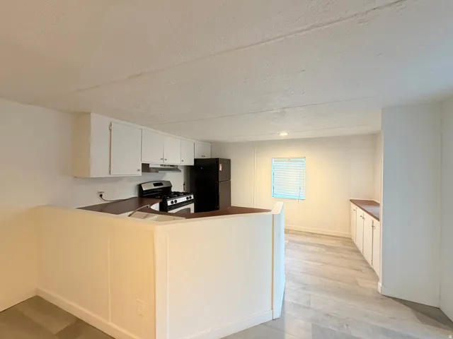 Kitchen featuring white cabinetry, dark countertops, a stainless steel range, and a black refrigerator