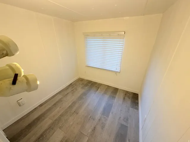 Room featuring wood-finish flooring, white walls, and a window with horizontal blinds
