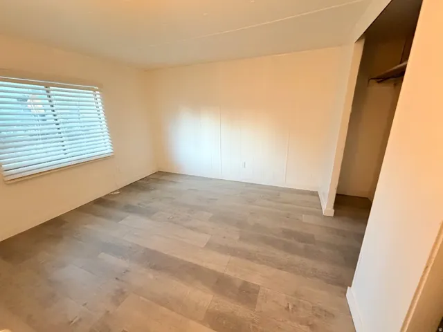 Bedroom featuring wood-finish flooring, a window with horizontal blinds, and a built-in closet with shelving
