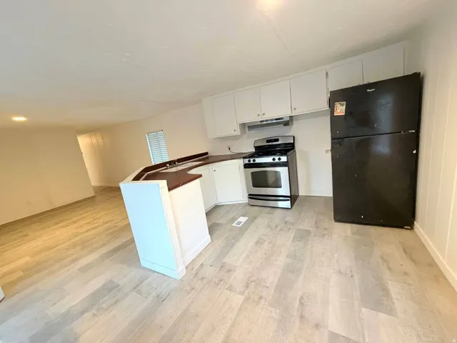 Open-concept kitchen featuring light wood-finish flooring, white cabinetry, a built-in stainless steel range, and a breakfast bar with a sink and wood-finish countertop