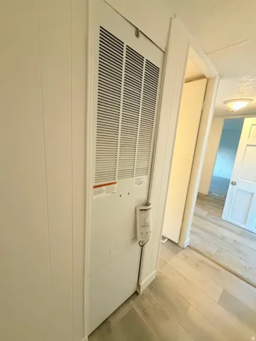 White utility closet with louvered vent, integrated control panel, and wood-finish flooring