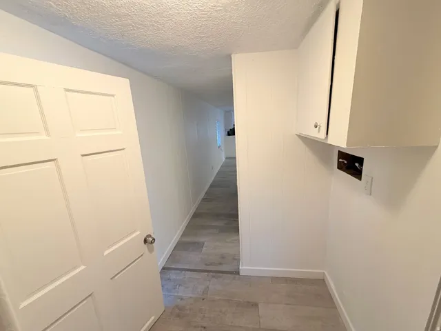 Laundry area featuring overhead cabinetry, wood-finish flooring, and white panel walls