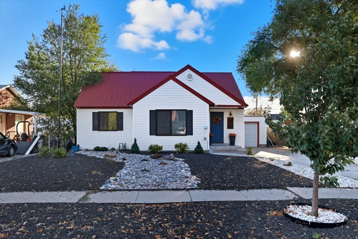 White siding residence featuring a bold red metal roof, black window shutters, a vibrant blue entry door, and an attached garage with a drive