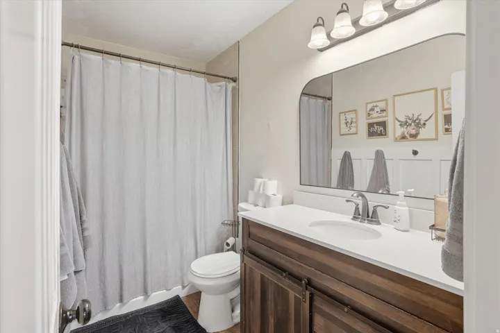 Bathroom featuring a wood-finish vanity with a white countertop, an oval undermount sink, and a framed mirror with an overhead light fixture