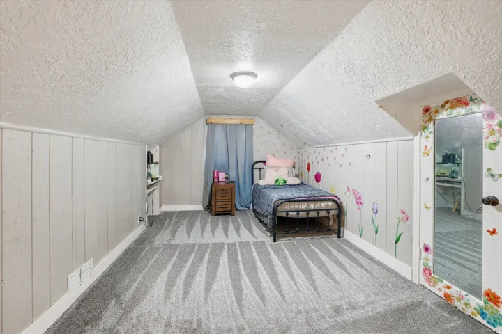 Carpeted room featuring sloped ceilings, textured white walls, and a flush-mount ceiling light