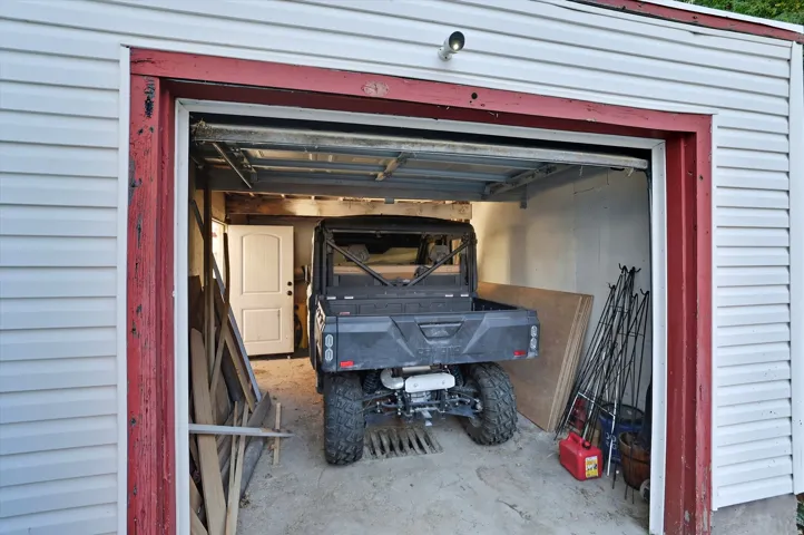 Detached garage with white vinyl siding, a red trim frame, and an exposed garage door track system