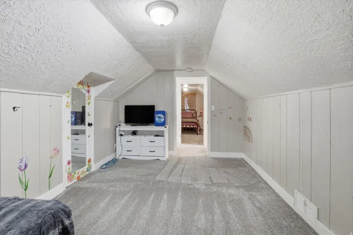 Carpeted room featuring sloped ceilings and light-colored panel walls