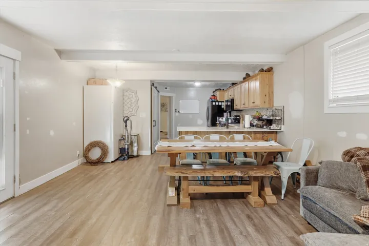 Open-concept living space featuring wood-finish flooring, exposed ceiling beams, and a kitchen with wood cabinetry