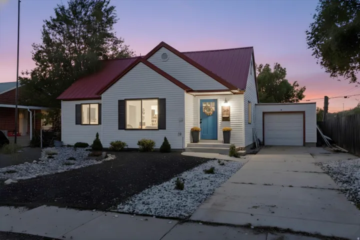 White siding exterior with a red metal roof, featuring a vibrant blue front door and dark-framed windows with decorative shutters