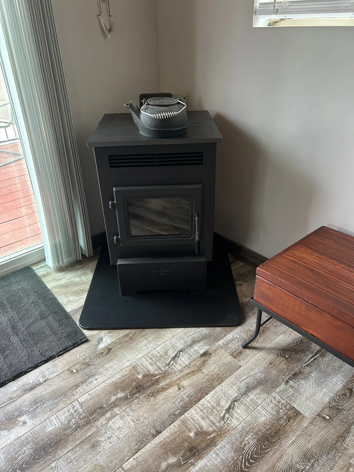 Freestanding black stove with a glass-front door and protective hearth pad