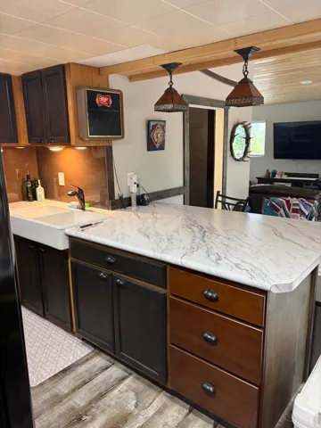 Kitchen featuring a farmhouse sink, dark wood-finish cabinetry, and a light-toned, veined countertop