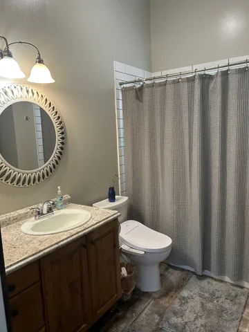 Bathroom featuring a wood-finish vanity with an integrated sink and light-toned countertop, a decorative round mirror, and a shower area with white subway tile surround