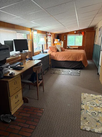 Spacious room featuring wood-paneled walls, multiple windows with blinds, and textured drop ceiling panels
