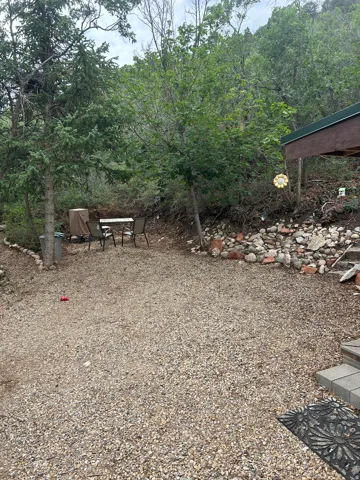 Gravel outdoor area featuring a compact patio set, natural stone steps, and a lush, tree-lined hillside backdrop
