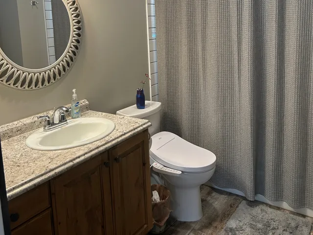 Bathroom featuring a single vanity with wood-finish cabinetry, a white porcelain sink, and a granite-look countertop