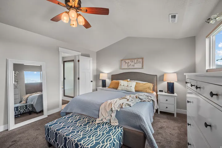 Carpeted bedroom featuring a vaulted ceiling and a ceiling fan with light fixture