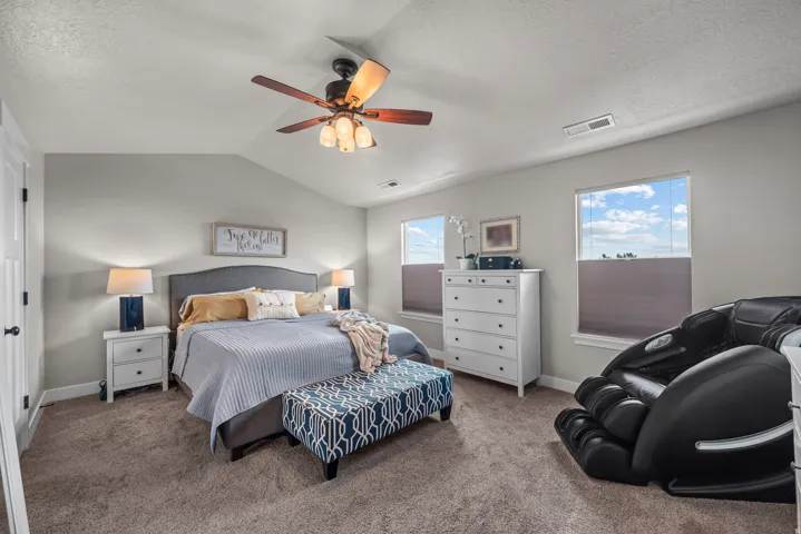 Carpeted bedroom featuring a vaulted ceiling and two windows with blinds