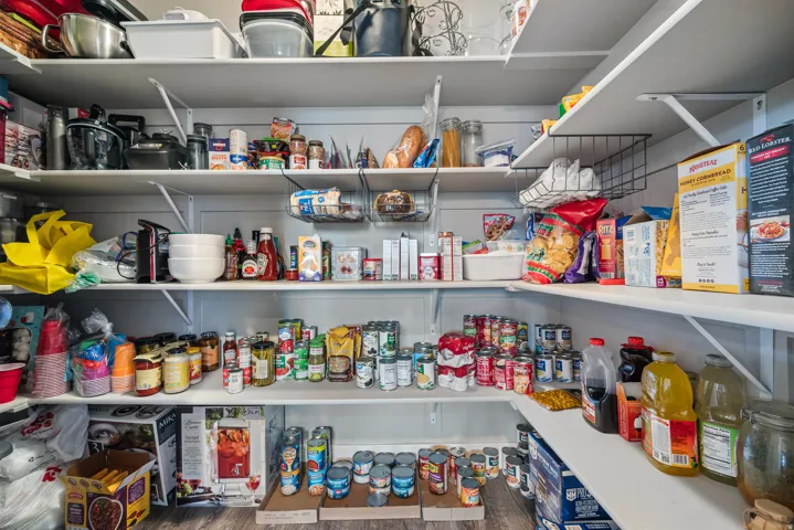 Spacious walk-in pantry featuring extensive white shelving, L-shaped configuration, and wood-finish flooring