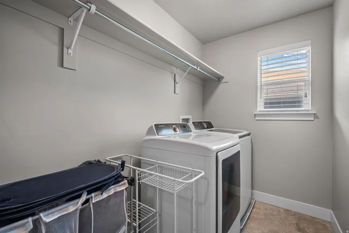 Utility space featuring a window with blinds, upper shelving with a hanging rod, and light-toned flooring