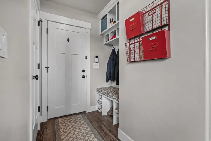 Entryway featuring a white paneled door with black hardware, built-in shelving, a bench with cushioned seating, and wood-finish flooring