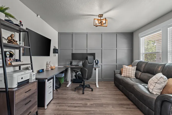 Dedicated room featuring wood-finish flooring, a contemporary ceiling light fixture, and a paneled accent wall