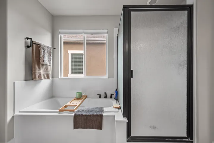 Contemporary bathroom featuring a built-in soaking tub with a tiled surround, a sliding window, and a separate shower enclosure with a dark-framed frosted glass door