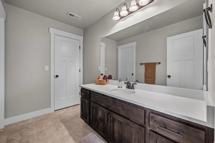Vanity with a white countertop and integrated sink, dark wood-finish cabinetry, and bronze-finish hardware