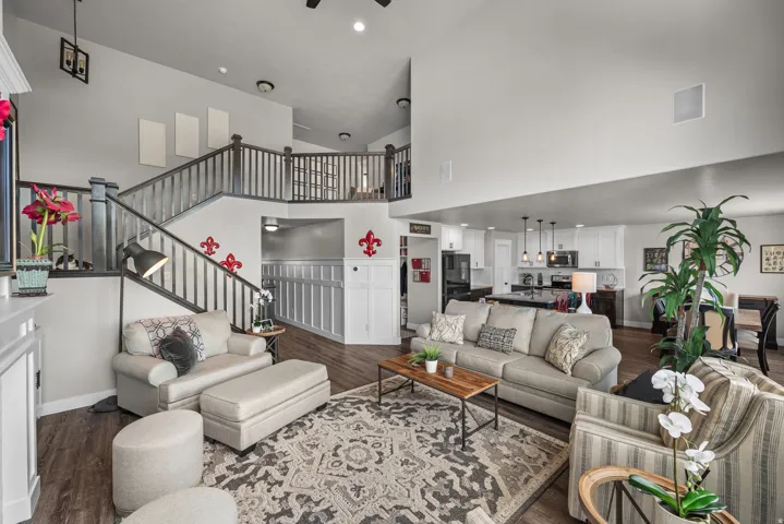 Open-concept living space featuring wood-finish flooring, a two-story ceiling, and a prominent staircase with dark wood railings