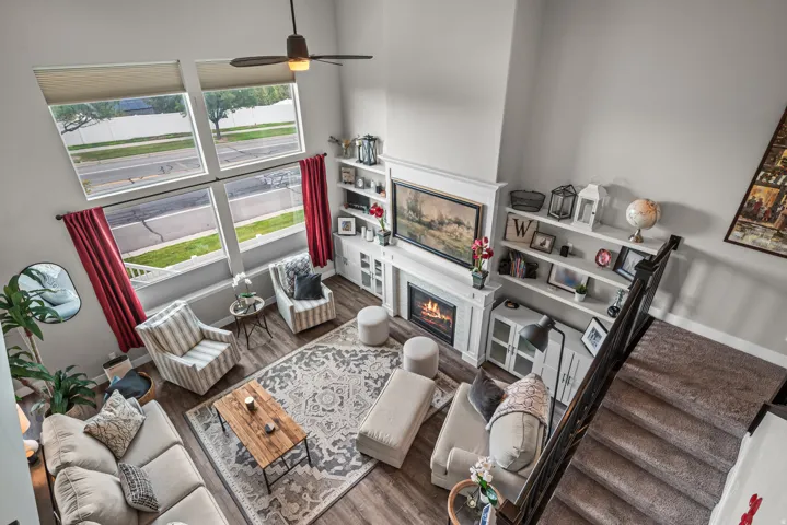 Two-story living area featuring a fireplace with white mantel, built-in shelving, wood-finish flooring, and a ceiling fan