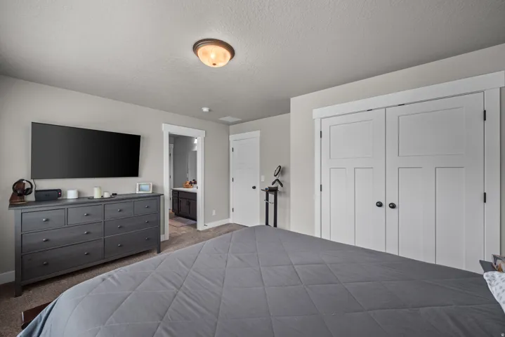 Bedroom with light gray walls, plush carpet flooring, a ceiling-mounted light fixture, and white bi-fold closet doors with black hardware