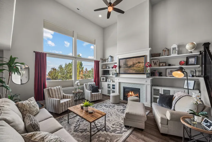 High ceilings featuring large windows with window treatments, a fireplace with a light-colored tile surround and white mantel, built-in shelving, and wood-finish flooring