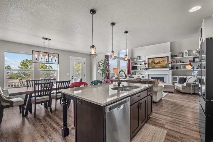 Open-concept living space with wood-finish flooring, a kitchen island with integrated sink, pendant lighting, and a dining area with a linear chandelier