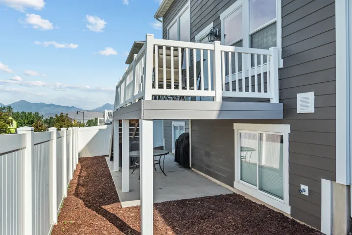 Upper-level balcony with white railing, lower-level patio, and dark gray horizontal siding