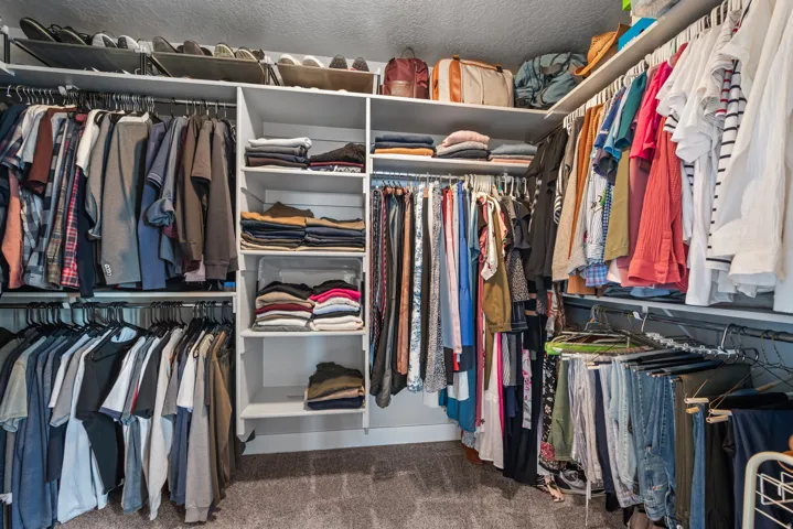 Walk-in closet featuring extensive built-in shelving, multiple hanging rods, and carpet flooring