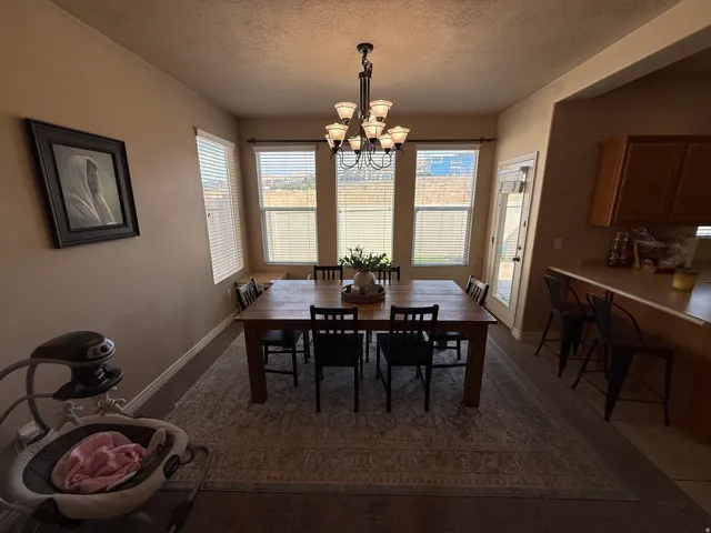 Dining area featuring a wood-finish dining table and six chairs, illuminated by a multi-bulb chandelier