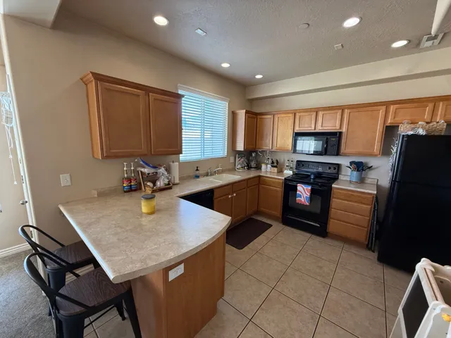 Functional kitchen featuring a peninsula with seating, wood-finish cabinetry, black appliances, tile flooring, and recessed lighting