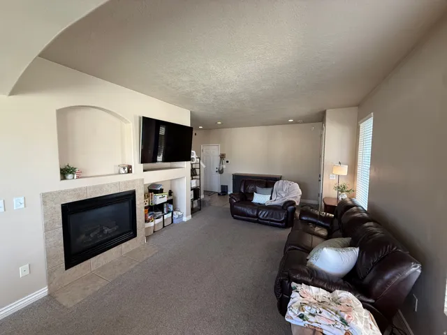 Living room featuring a gas fireplace with a tiled surround, an arched wall niche, built-in shelving, carpet flooring, and neutral wall tones