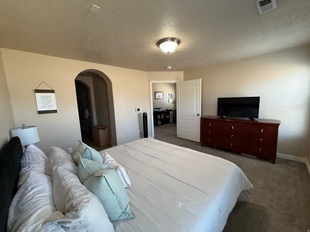 Spacious room featuring neutral-toned walls, a carpeted floor, and an arched doorway leading to an additional space