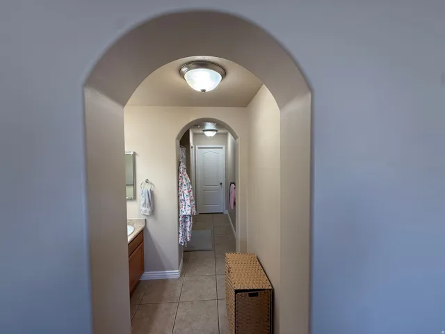Archway entry to a hallway featuring tile flooring, a single vanity with a mounted mirror, and a white paneled door
