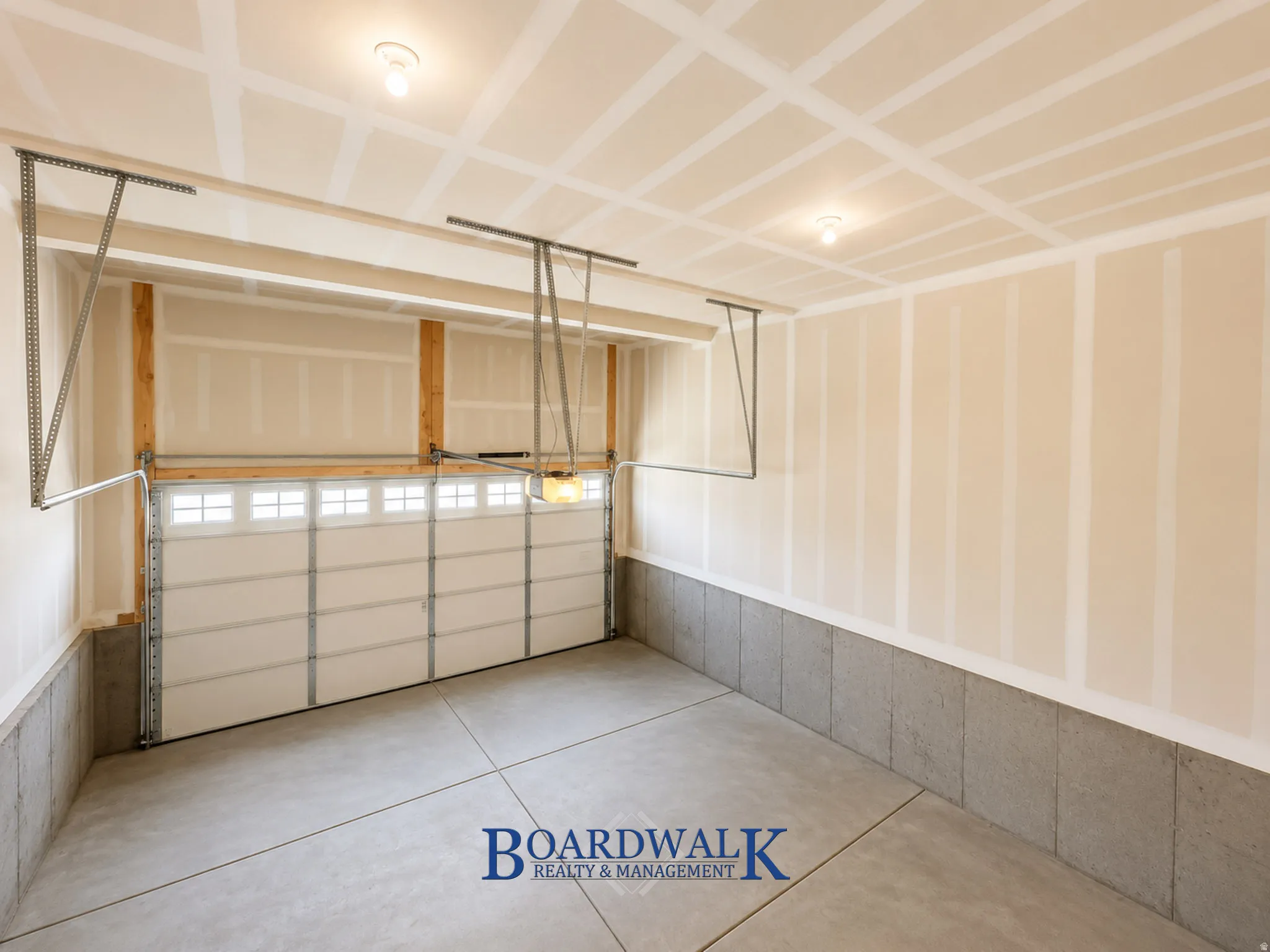 Spacious garage featuring a sectional overhead door with upper window panels, exposed wood framing, concrete flooring, and built-in overhead lighting