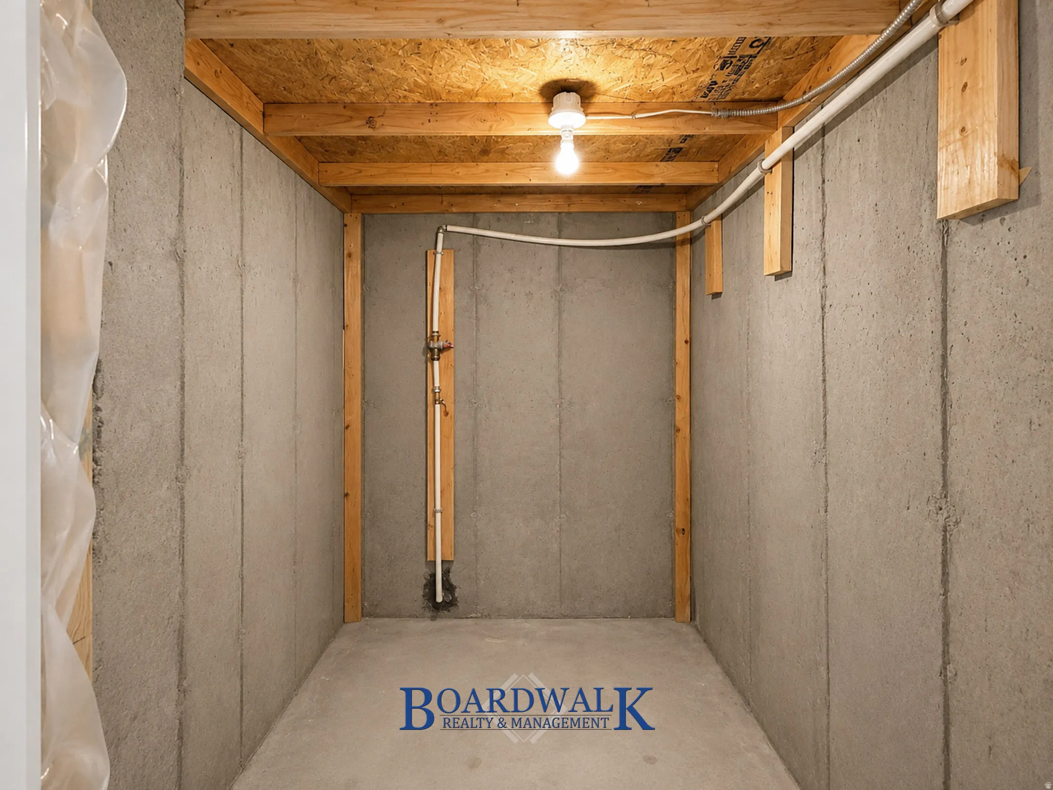 Unfinished room featuring concrete walls and flooring, exposed wood ceiling joists, and overhead lighting