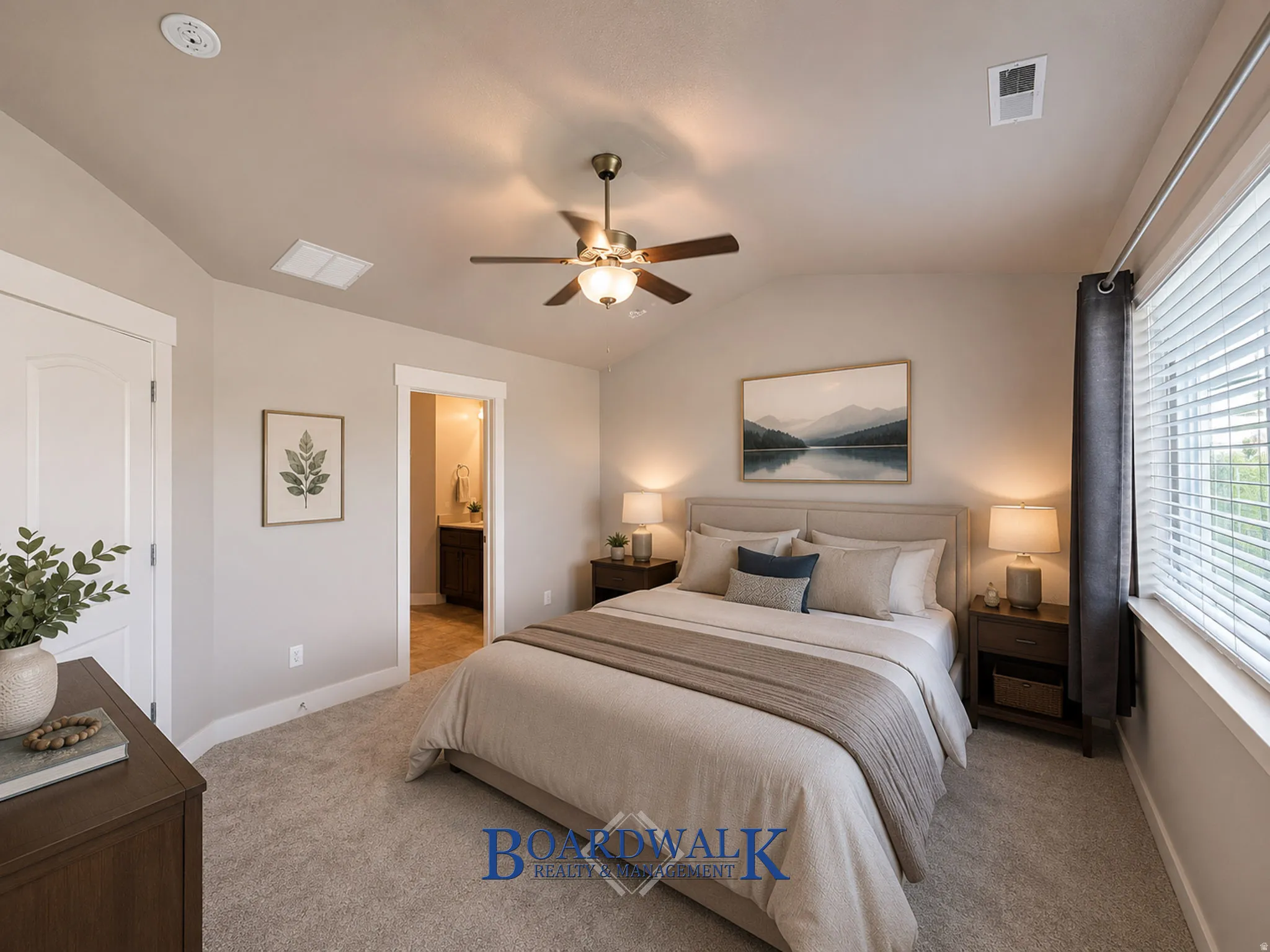 Carpeted bedroom featuring a vaulted ceiling with a ceiling fan, a window with horizontal blinds, and an entryway to a bathroom with a vanity and mirror